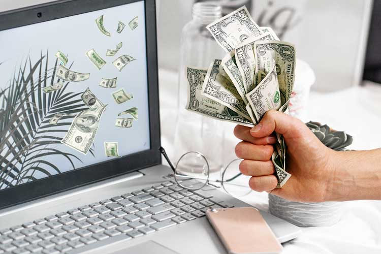 A person holding a stack of money in front of a laptop